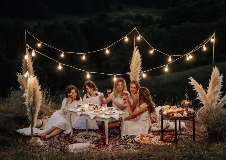 Frauen bei einem schicken Picknick in der Natur bei Abend mit Lichterkette