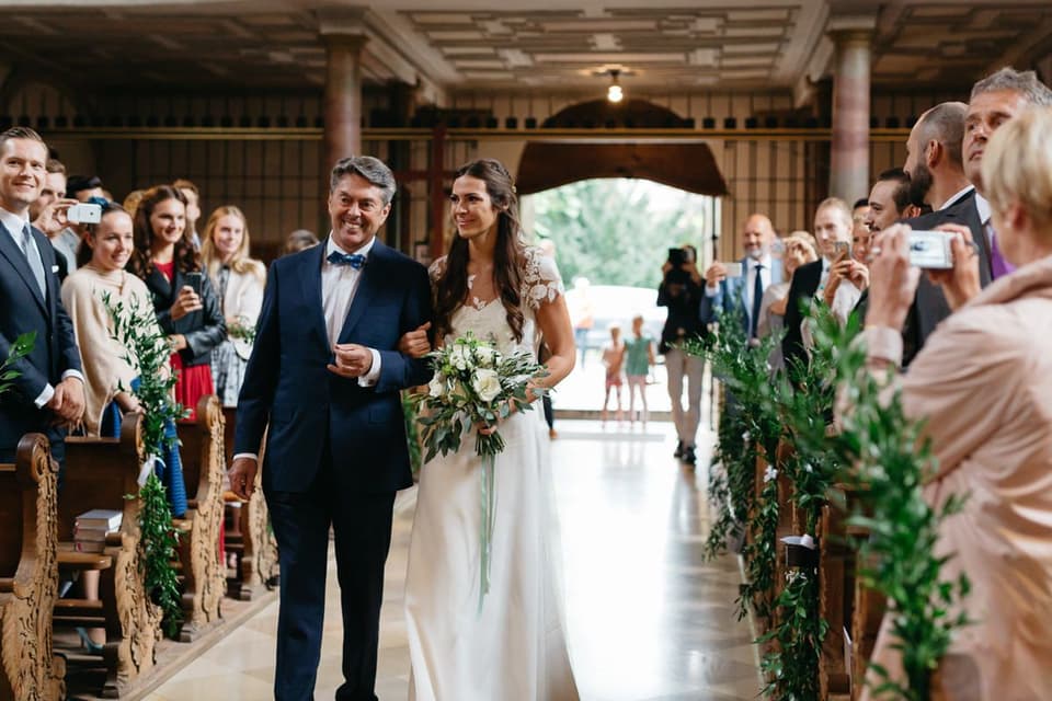 Die Braut wird von ihrem Vater zum Altar geführt und hält in ihrer freien Hand den Brautstrauß.