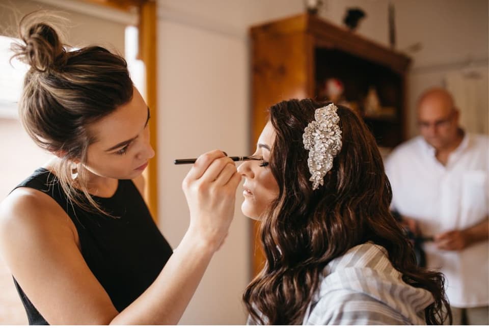 Die Braut wird von ihrer Stylistin geschminkt.