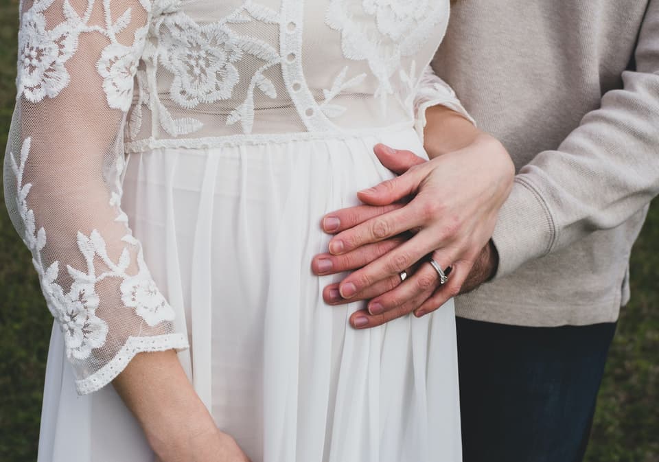 Braut und Bräutigam haben Hände auf dem Babybauch