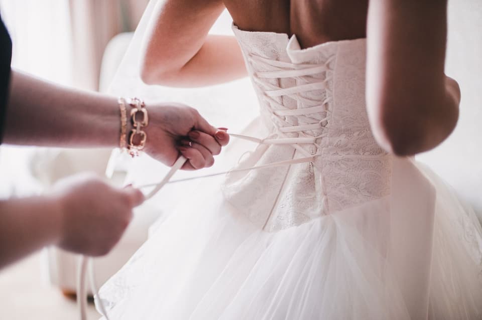 Jemand schnürt der Braut die Corsage am Kleid