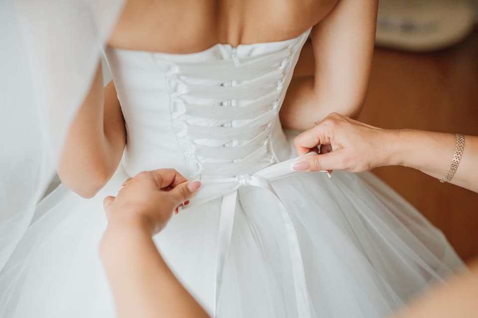 Einer Braut wird die Corsage am Kleid geschnürt