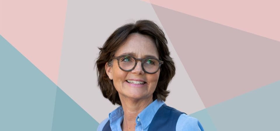 Eine Frau mit Brille lächelt vor einem bunten Hintergrund.