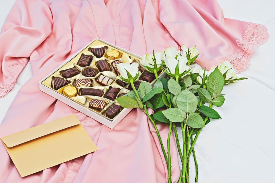 Ein rosafarbenes Gewand mit einer Schachtel Pralinen und Blumen.