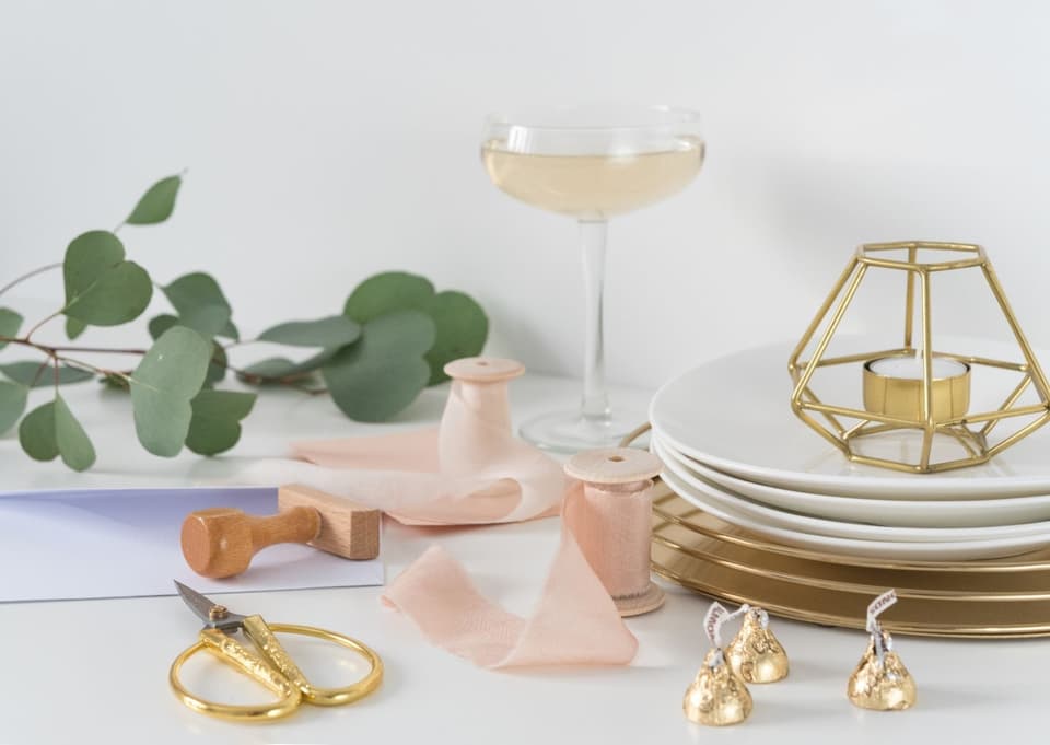 Stempelset für die Hochzeit auf einem Tisch mit Geschirr, Schere und rosa Bänder