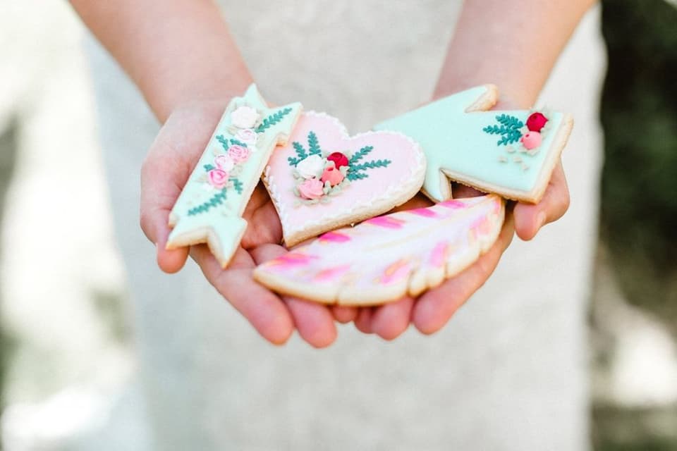Eine Braut hält mit Blumen und Pfeilen verzierte Kekse in der Hand.