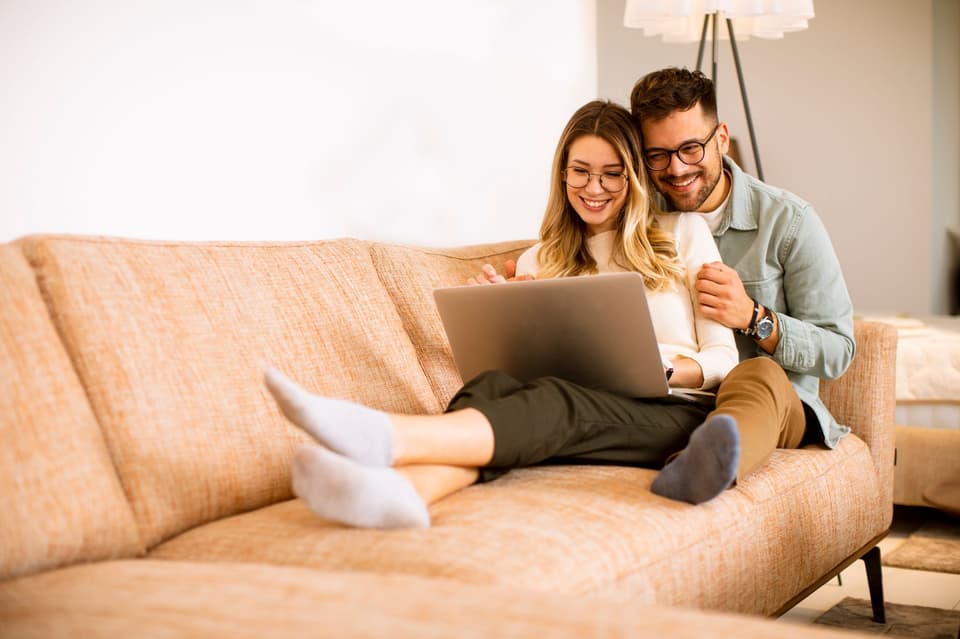 Ein Paar sitzt auf einer Couch und benutzt einen Laptop.