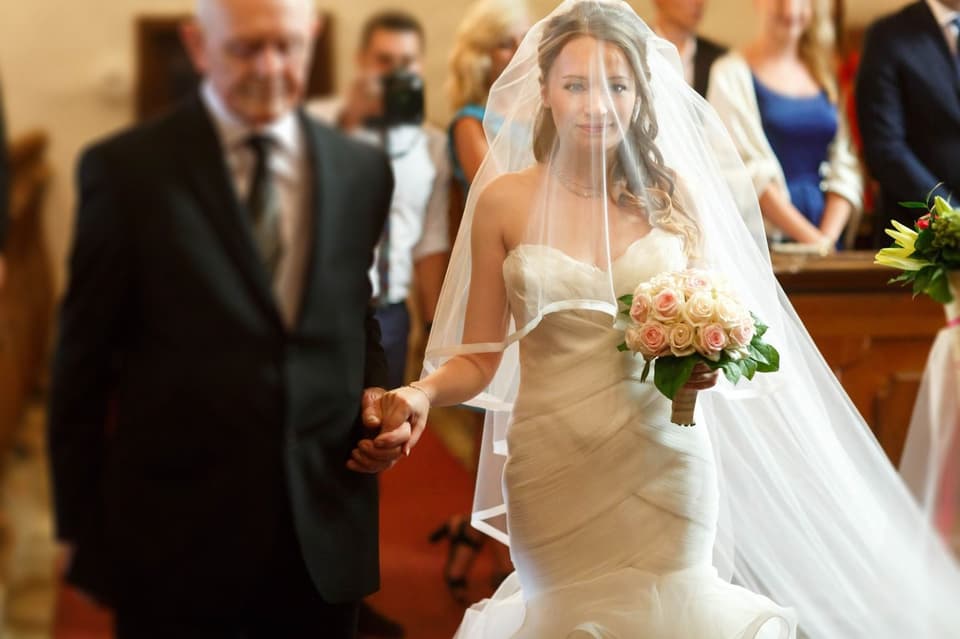 Braut schreitet mit Brautstrauß in der Hand auf ihrer Hochzeit den Gang entlang
