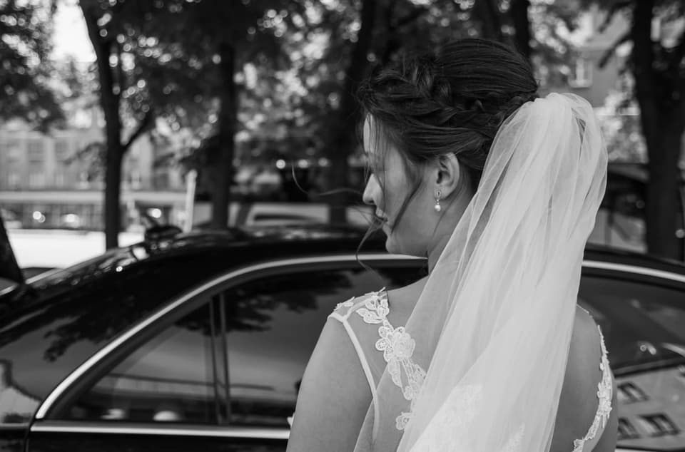 Braut mit Schleier steht vor dem Hochzeitsauto