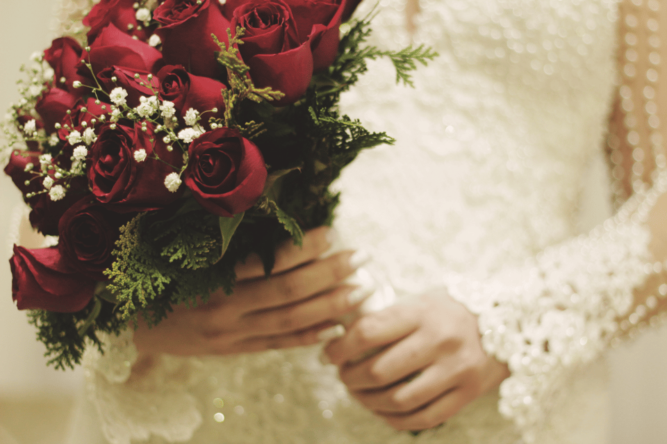 Eine Braut hält einen Brautstrauß aus roten Rosen und weißen Schleierkraut.
