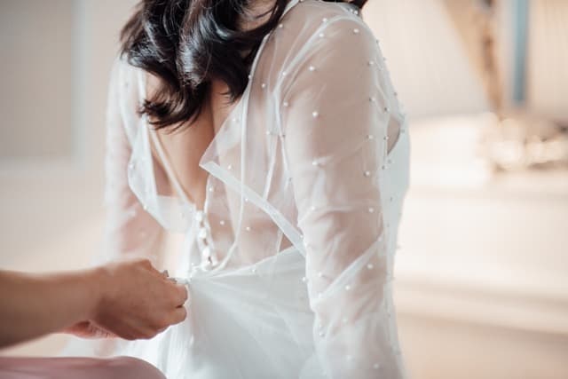 Jemand hilft der Braut beim Anziehen am Hochzeitsmorgen