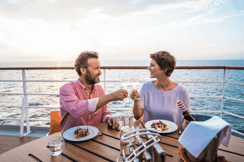 Paar stößt beim Abendessen an, im Hintergrund das weite Meer.