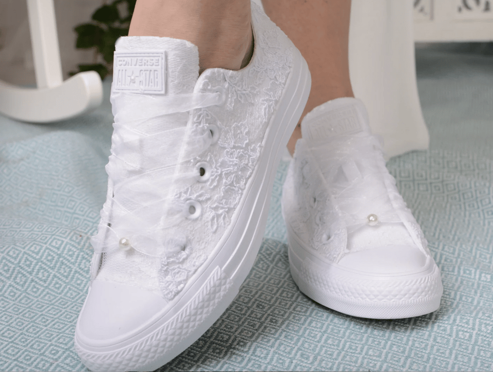 Eine Frau trägt weiße Converse-Schuhe mit Spitze und Perlen.