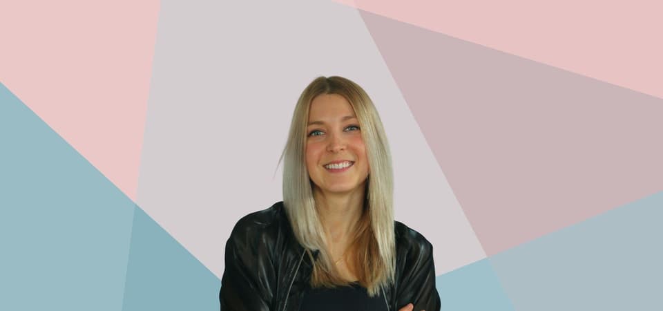 Eine Frau in einer schwarzen Jacke lächelt vor einem rosa-blauen Hintergrund.